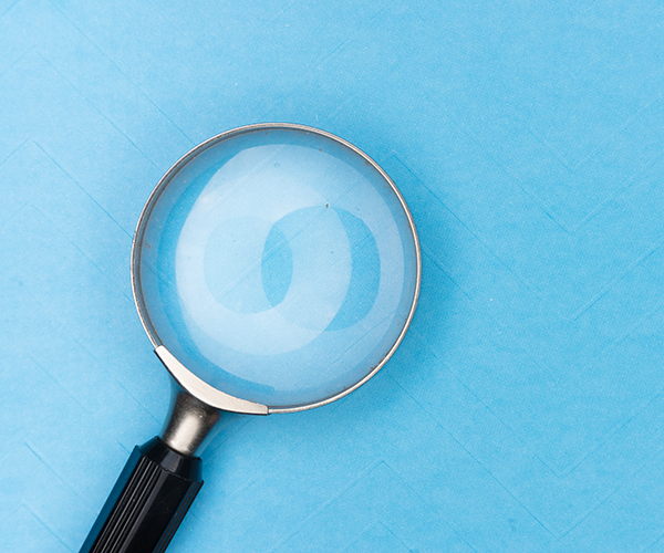 A handheld magnifying glass lies against a sky blue background